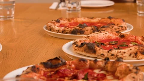Server Placing Multiple Neapolitan Pizzas on a Wooden Restaurant Table Stock Footage 337767577
