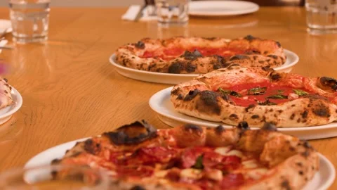 Server Placing Multiple Neapolitan Pizzas on a Wooden Restaurant Table Stock Footage 337860371