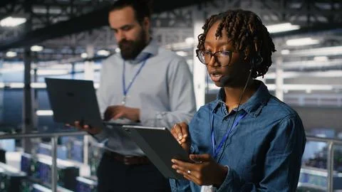 Server room admin uses tablet and headset to provide infrastructure tech support Stock Photos