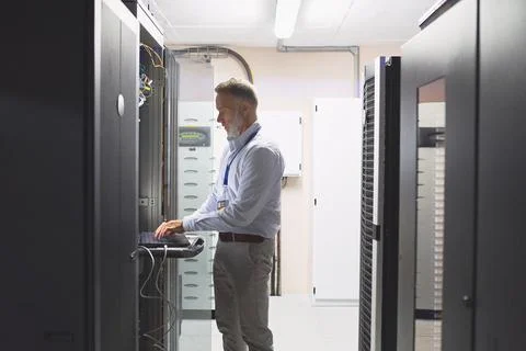 Server room, engineer and typing with laptop for cybersecurity, maintenance or Stock Photos