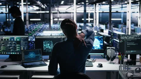 Server room technician stretching sore back while using AI at desk Stock Footage 313569717