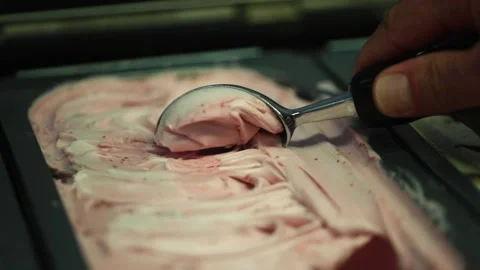 A Server scooping strawberry flavored gelato from tray inside gelato parlor Stock Footage 155453928