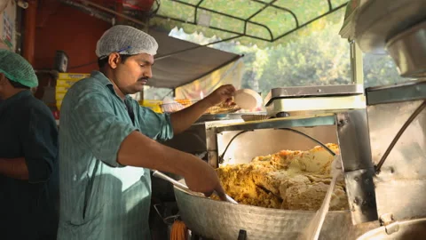 A server weighing and putting halwa in plates for breakfast. Stock Footage 220143691