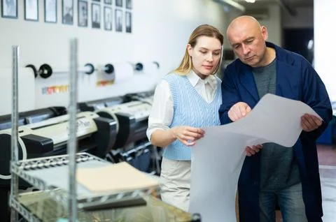 Service engineer and office worker checking printed document together against Foto stock