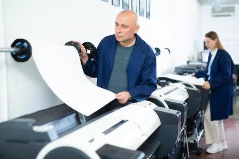 Service man uses plotter and checks functionality in printing shop Fotos de archivo