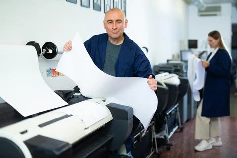 Service man uses plotter and checks functionality in printing shop Fotos de archivo