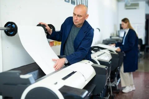 Service man uses plotter and checks functionality in printing shop Fotos de archivo