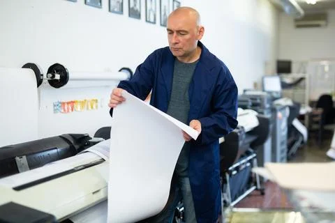 Service man uses plotter and checks functionality in printing shop Fotos de archivo