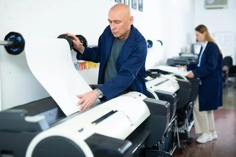 Service man uses plotter and checks functionality in printing shop Fotos de archivo