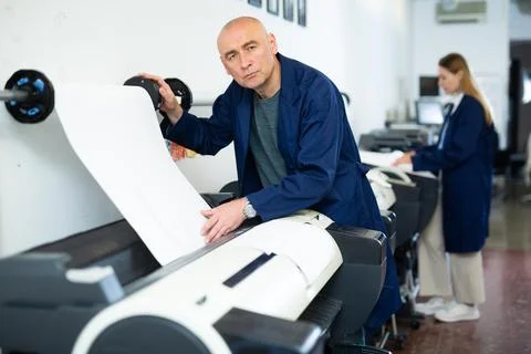 Service man uses plotter and checks functionality in printing shop Fotos de archivo