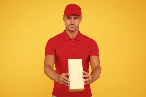 Service plus quality. Serious guy hold parcel yellow background. Man delivery 스톡 사진