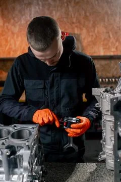 At a service station on the table young engine repairman puts a piston part in Stock Photos