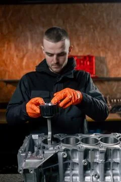 At a service station on the table young engine repairman puts a piston part in Stock Photos