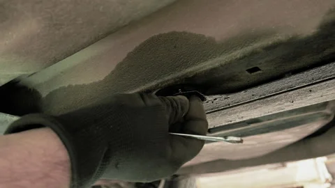 The service technician lies under the car and removes the screw with his fingers Stock Footage 196882575