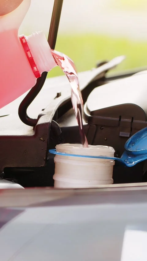 Service worker man pours car fluid windscreen red cleaning washer glass summer Stock Footage 323353901