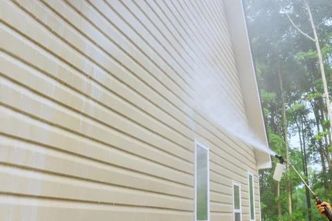 Service worker utilizes high pressure nozzles to efficiently clean siding houses Stock Photos