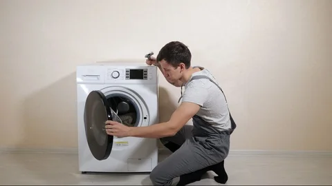 Serviceman repairs broken washing machine near beige wall Stock Footage 121566499