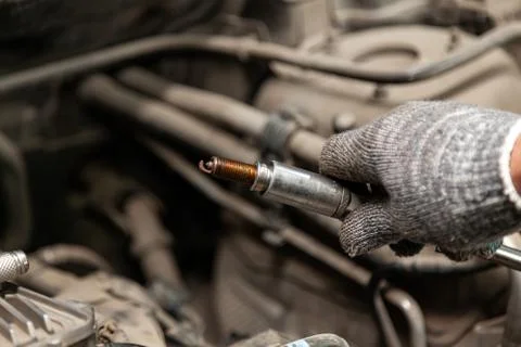 A serviceman repairs a car while replacing the spark plugs while holding one  Stock Photos