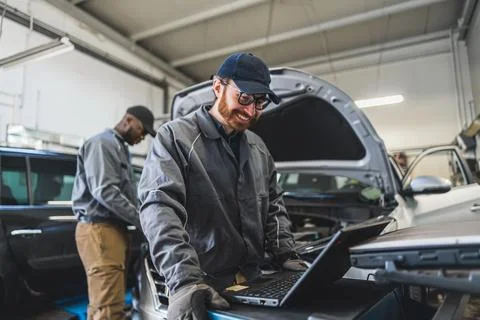 Servicemen completing car engine diagnostics with laptop in a repair shop 스톡 사진
