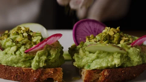 Serving avocado toast, putting slices of radish in squeezed avocado macro shot Stock Footage 128483064