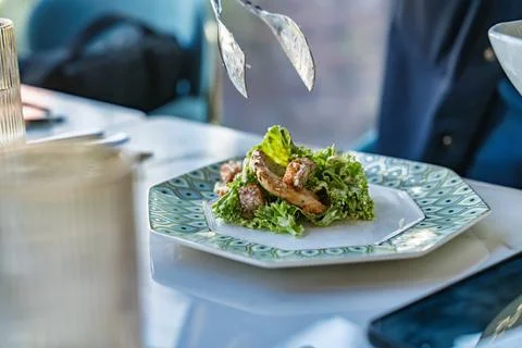 Serving delicious chicken caesar salad with tongs in restaurant Stock Photos
