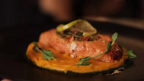 Serving of dish with smoked salmon on mashed carrots puree on black plate Video stock 259985004