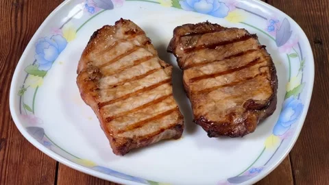 Serving of grilled pork steaks on plate on rustic table Stock Footage 345670024