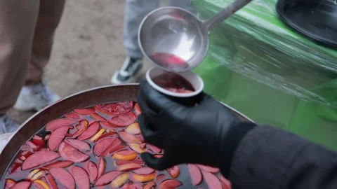 Serving hot mulled wine with apple slices from large bowl in outdoor setting Stock Footage 300206545
