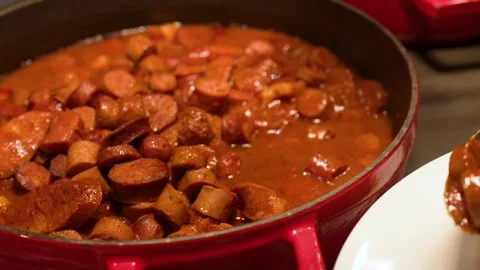 Serving Hot Sausage Stew from a Red Pot onto a White Plate Stock Footage 334919262