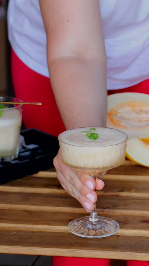 Serving melon cocktail with white wine and ice in elegant coupe glass with mint, Stock Footage 313794011