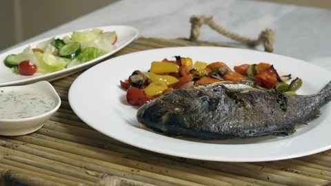 Serving roasted sea bream fish with with vegetables, sauce, and fresh salad Stock-Footage 122233265