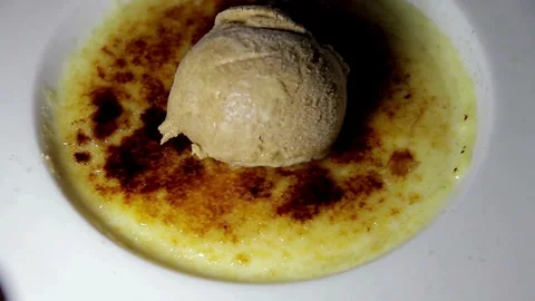Serving scoop of ice cream on top of creme brulee dessert Video stock 336229848