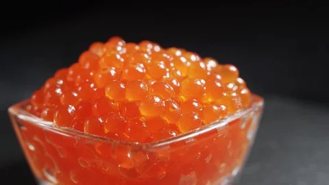 A serving of selected red caviar rotates on a black background in a transparent Video stock 123410818