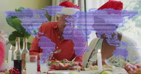Serving senior pair wearing red Santa hats passing salad at dining table, purple Stock Photos