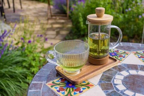 Serving tea with a teapot in a rustic bistro with a vium in flover's garden Stock Photos