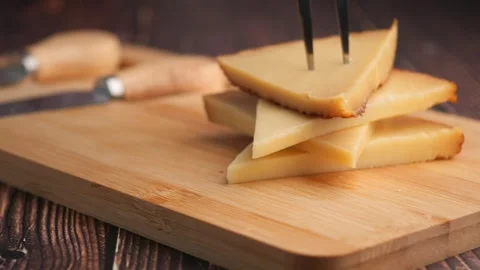 Serving triangular manchego cheese slices from wooden board using stainless.. 스톡 동영상 332408506