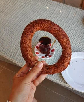 Sesame simit held above tea glass on table. Turkish breakfast ritual, tradi.. 스톡 사진