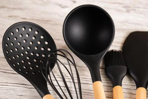 Set of black silicone kitchen utensils with wooden handles on wooden backgrou Stock Photos