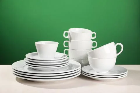 Set of clean dishware on white table against green background Foto stock