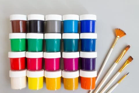 A set of closed jars with gouache of different colors and brushes on a gray Stock Photos