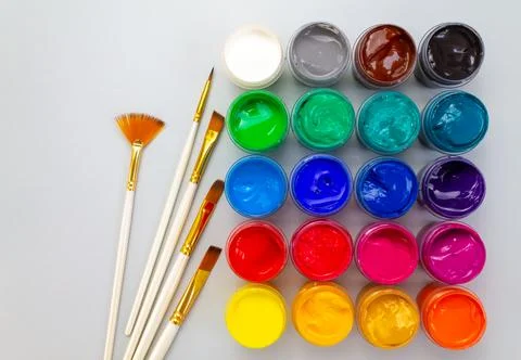 A set of closed jars with gouache of different colors and brushes on a gray Stock Photos