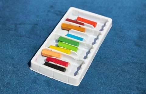 Set of colored crayons in a white box lies on a blue surface Stock Photos