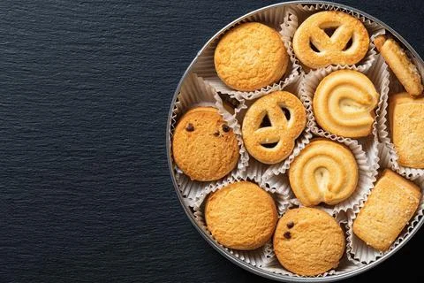 Set of crispy shortbread biscuits in an open tin over black slate surface. Stock Photos