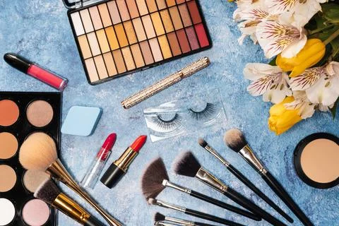 A set of decorative cosmetics, makeup brushes and a bouquet of flowers on a blue Stock Photos