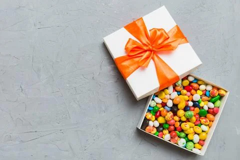 Set of different sweet candy in a paper box with a satin ribbon on a colore.. Stock Photos