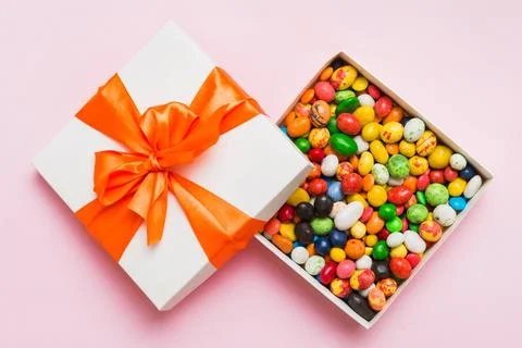 Set of different sweet candy in a paper box with a satin ribbon on a colore.. Stock Photos