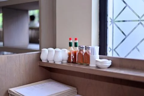 Set of dining condiments including white salt shakers, hot sauce bottles, s.. Stock Photos