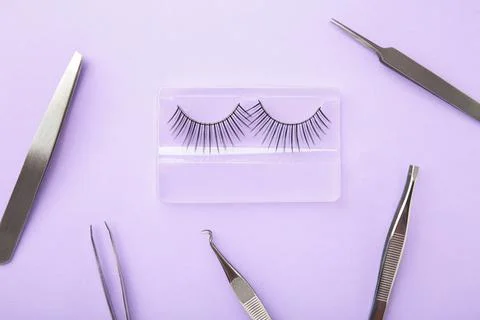 Set of false eyelashes extencions on purple background with tweezers. Minimal Stock Photos