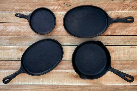 Set of four round &amp; oval cast iron skillets of different sizes on a wooden deck Stock Photos
