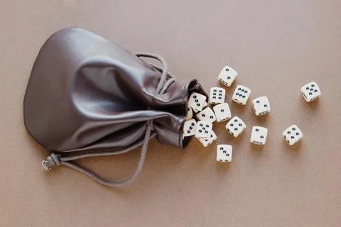 Set of gaming dice rolled out of leather bag on brown background. Concept wit Stock Photos